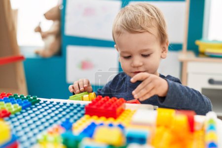 Photo for Adorable blond toddler playing with construction blocks standing at kindergarten - Royalty Free Image
