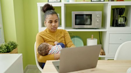 Foto de Madre e hijo trabajador de negocios que trabaja en línea mientras amamanta al bebé en el comedor - Imagen libre de derechos