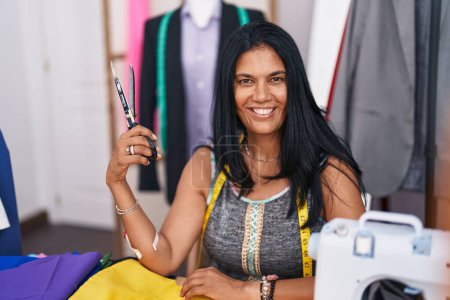 Téléchargez les photos : Femme hispanique du Moyen Age tailleur souriant confiant tenant des ciseaux au magasin de tailleur - en image libre de droit