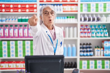 Photo for Middle age woman with tattoos working at pharmacy drugstore pointing with finger surprised ahead, open mouth amazed expression, something on the front - Royalty Free Image