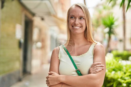 Téléchargez les photos : Jeune femme blonde souriante confiante debout avec les bras croisés geste à la rue - en image libre de droit
