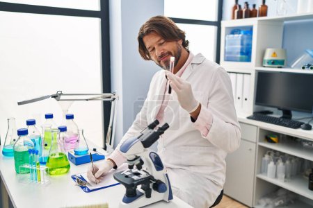 Téléchargez les photos : Homme d'âge moyen scientifique tenant tube à essai sanguin écrit sur le document au laboratoire - en image libre de droit