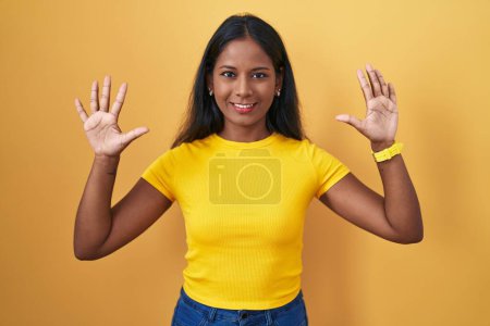 Téléchargez les photos : Jeune femme indienne debout sur fond jaune montrant et pointant vers le haut avec les doigts numéro dix tout en souriant confiant et heureux. - en image libre de droit
