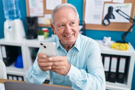 Foto de Trabajador de negocios hombre de pelo gris de mediana edad usando un teléfono inteligente que trabaja en la oficina - Imagen libre de derechos