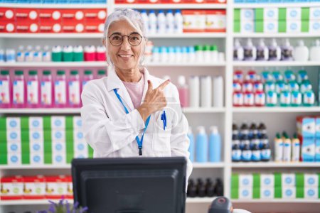 Photo for Middle age woman with tattoos working at pharmacy drugstore cheerful with a smile on face pointing with hand and finger up to the side with happy and natural expression - Royalty Free Image