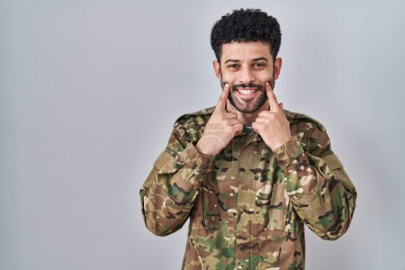 Photo for Arab man wearing camouflage army uniform smiling with open mouth, fingers pointing and forcing cheerful smile - Royalty Free Image