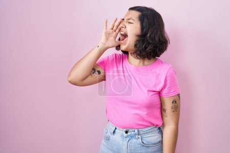 Téléchargez les photos : Jeune femme hispanique debout sur fond rose criant et criant fort à côté avec la main sur la bouche. concept de communication. - en image libre de droit