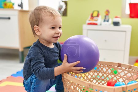Photo for Adorable blond toddler playing with balls sitting on floor at kindergarten - Royalty Free Image
