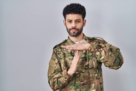 Foto de Hombre árabe vistiendo uniforme camuflaje ejército haciendo tiempo fuera gesto con las manos, rostro frustrado y serio - Imagen libre de derechos
