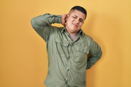 Téléchargez les photos : Jeune homme hispanique debout sur fond jaune souffrant de douleurs au cou, toucher le cou avec la main, douleurs musculaires - en image libre de droit