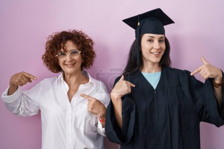 Photo for Hispanic mother and daughter wearing graduation cap and ceremony robe looking confident with smile on face, pointing oneself with fingers proud and happy. - Royalty Free Image