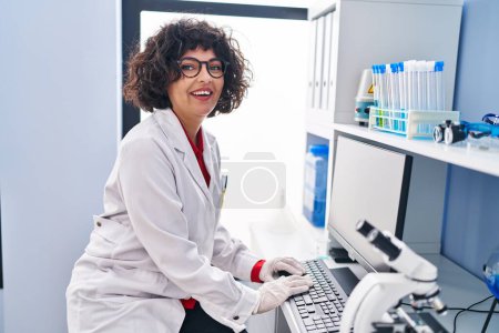 Téléchargez les photos : Jeune belle femme hispanique scientifique souriant confiant en utilisant l'ordinateur au laboratoire - en image libre de droit