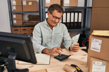 Foto de Middle age man ecommerce business worker counting dollars at office - Imagen libre de derechos