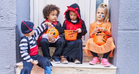 Photo for Group of kids wearing halloween costume putting sweets in pumpkin basket at street - Royalty Free Image