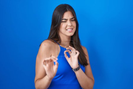 Photo for Hispanic woman standing over blue background disgusted expression, displeased and fearful doing disgust face because aversion reaction. - Royalty Free Image