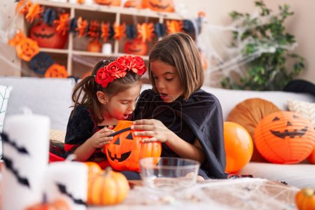 Foto de Adorable niño y niña con disfraz de halloween mirando en la cesta de calabaza en casa - Imagen libre de derechos