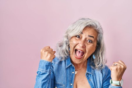 Téléchargez les photos : Femme d'âge moyen avec les cheveux gris debout sur fond rose très heureux et excité faisant geste gagnant avec les bras levés, souriant et criant pour le succès. concept de célébration. - en image libre de droit