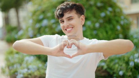 Téléchargez les photos : Homme non binaire souriant confiant faire geste de coeur avec les mains au parc - en image libre de droit