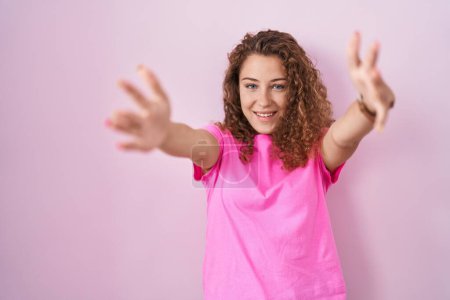 Téléchargez les photos : Jeune femme caucasienne debout sur fond rose regardant la caméra souriant à bras ouverts pour étreindre. expression joyeuse embrassant le bonheur. - en image libre de droit
