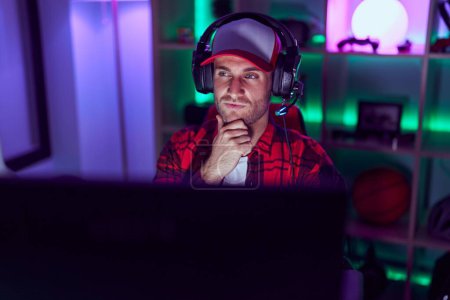 Photo for Young caucasian man playing video games serious face thinking about question with hand on chin, thoughtful about confusing idea - Royalty Free Image