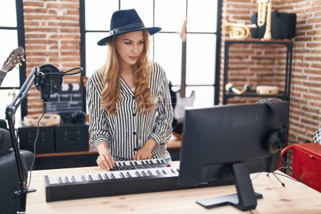 Foto de Young blonde woman musician playing piano keyboard at music studio - Imagen libre de derechos