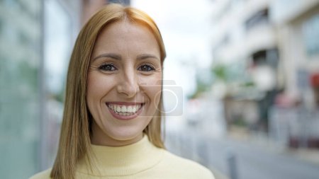 Foto de Joven mujer rubia sonriendo confiada de pie en la calle - Imagen libre de derechos