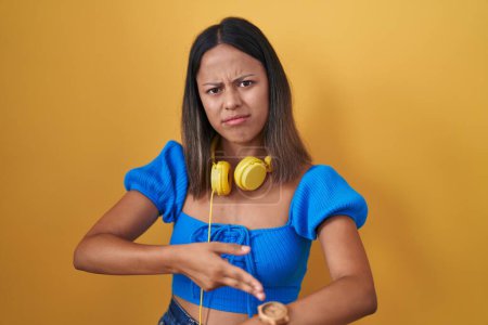 Téléchargez les photos : Jeune femme hispanique debout sur fond jaune à la hâte pointant pour regarder le temps, l'impatience, bouleversé et en colère pour retard de délai - en image libre de droit