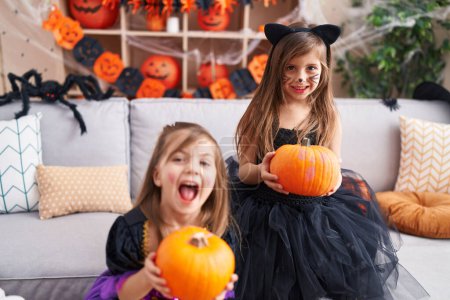 Téléchargez les photos : Adorables filles ayant fête d'Halloween tenant citrouille à la maison - en image libre de droit