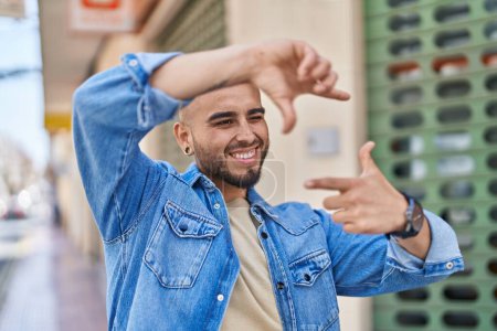 Foto de Young hispanic man smiling confident doing photo gesture with hands at street - Imagen libre de derechos