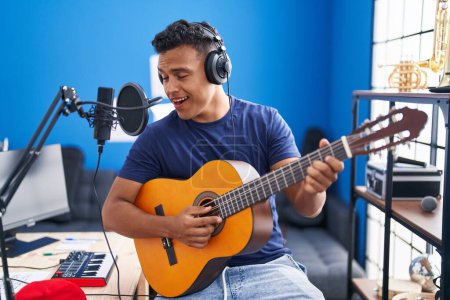 Foto de Young latin man musician singing song playing classical guitar at music studio - Imagen libre de derechos