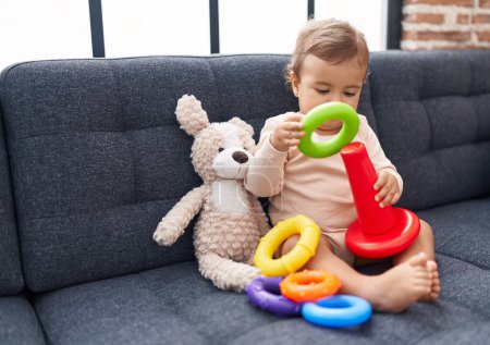 Téléchargez les photos : Adorable bébé hispanique jouant avec cerceaux jeu assis sur le canapé à la maison - en image libre de droit