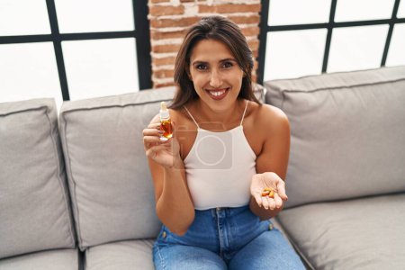 Photo for Young hispanic woman holding pills and cbd oil smiling with a happy and cool smile on face. showing teeth. - Royalty Free Image