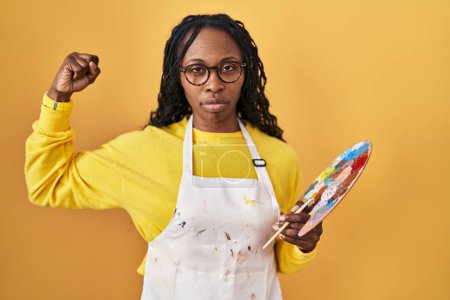 Téléchargez les photos : Femme africaine tenant palette peintre personne forte montrant muscle du bras, confiant et fier de la puissance - en image libre de droit
