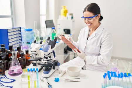 Photo for Young beautiful hispanic woman scientist smiling confident writing report working at laboratory - Royalty Free Image