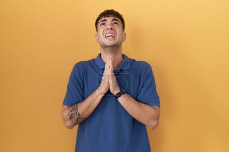 Photo for Young hispanic man standing over yellow background begging and praying with hands together with hope expression on face very emotional and worried. begging. - Royalty Free Image