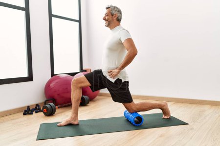 Photo for Middle age grey-haired man using foam roller stretching at sport center - Royalty Free Image