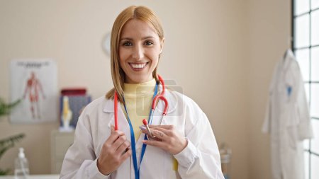 Téléchargez les photos : Jeune femme blonde médecin souriant confiant debout à la clinique - en image libre de droit