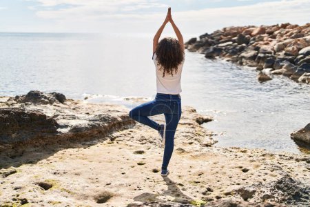 Téléchargez les photos : Young hispanic woman doing yoga exercise standing on back view at seaside - en image libre de droit