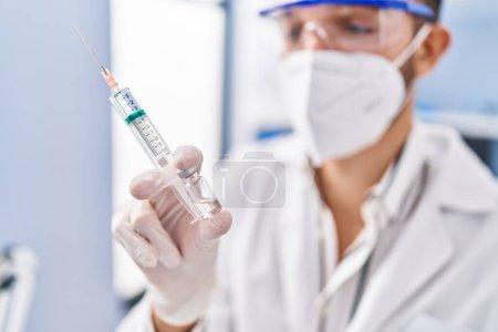 Photo for Young hispanic man scientist wearing medical mask holding covid vaccine at laboratory - Royalty Free Image