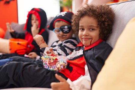 Foto de Grupo de niños con disfraz de Halloween comiendo caramelos en casa - Imagen libre de derechos