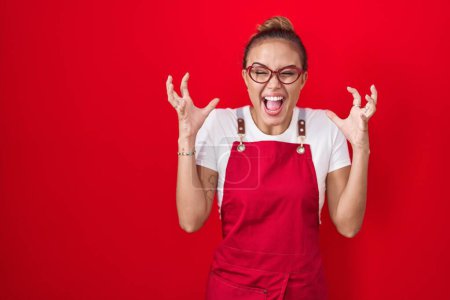 Photo for Young hispanic woman wearing waitress apron over red background celebrating mad and crazy for success with arms raised and closed eyes screaming excited. winner concept - Royalty Free Image