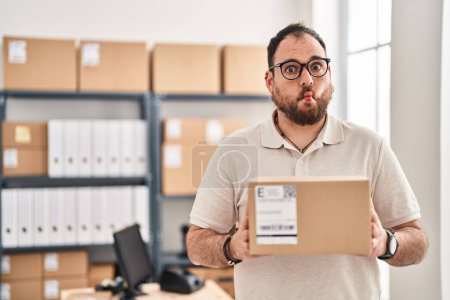 Photo for Plus size hispanic man with beard working at small business ecommerce making fish face with mouth and squinting eyes, crazy and comical. - Royalty Free Image