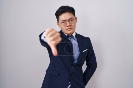 Téléchargez les photos : Jeune homme asiatique portant costume d'affaires et cravate regardant malheureux et en colère montrant rejet et négatif avec les pouces vers le bas geste. mauvaise expression. - en image libre de droit