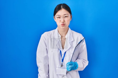 Téléchargez les photos : Jeune femme chinoise travaillant au laboratoire scientifique gonflant les joues avec un drôle de visage. bouche gonflée d'air, expression folle. - en image libre de droit