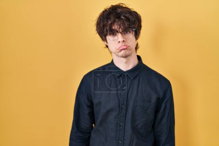 Foto de Joven con gafas sobre fondo amarillo deprimido y preocupado por la angustia, llorando enojado y asustado. expresión triste. - Imagen libre de derechos