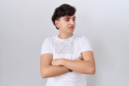 Téléchargez les photos : Jeune homme non binaire portant un t-shirt blanc décontracté regardant sur le côté avec les bras croisés convaincu et confiant - en image libre de droit