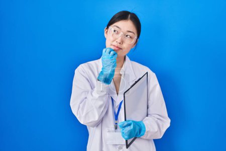 Photo for Chinese young woman working at scientist laboratory with hand on chin thinking about question, pensive expression. smiling with thoughtful face. doubt concept. - Royalty Free Image