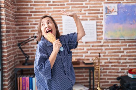 Téléchargez les photos : Femme d'âge moyen chantant chanson en utilisant la brosse comme un microphone à la maison - en image libre de droit
