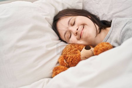 Photo for Young woman with down syndrome lying on bed sleeping with teddy bear at bedroom - Royalty Free Image