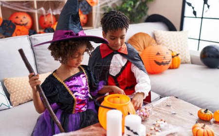 Foto de Adorable afroamericano chico y chica con disfraz de halloween sosteniendo caramelos de bol en casa - Imagen libre de derechos